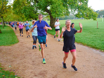 Runners participating in University Parks parkrun smile and wave at the camera